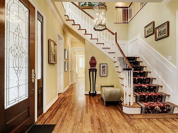 The reception hall and main floor hallway with a mahogany leaded glass front door with sidelights, decorative brass levered door handle, hardwood floors, crown molding, recessed lighting, 9-candle glass framed pendant light, quarter-turn stairway ele