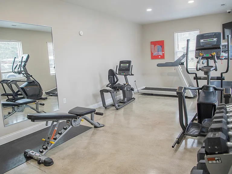 Modern apartment gym with state-of-the-art equipment, including a treadmill, elliptical, stationary bike, and free weights, in a bright and spacious setting.