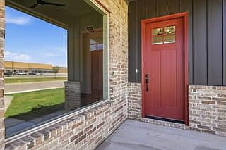 A red front door with a window and brick exterior is shown next to a large window reflecting the str