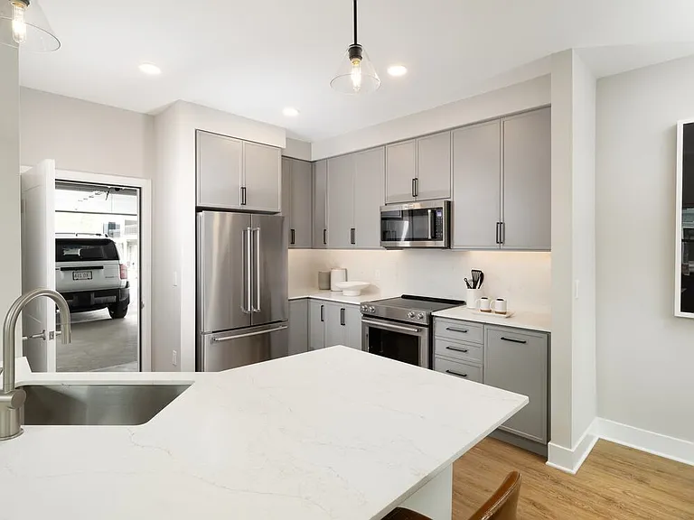 Signature Collection Townhome kitchen with upgraded stainless steel appliances, white quartz countertops and backsplash, grey cabinetry, hard surface flooring, and attached garage.