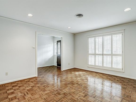 This view is looking back at the front door and Foyer from the Living Room with recessed lighting and plantation shutters on the large window which overlooks the front yard.