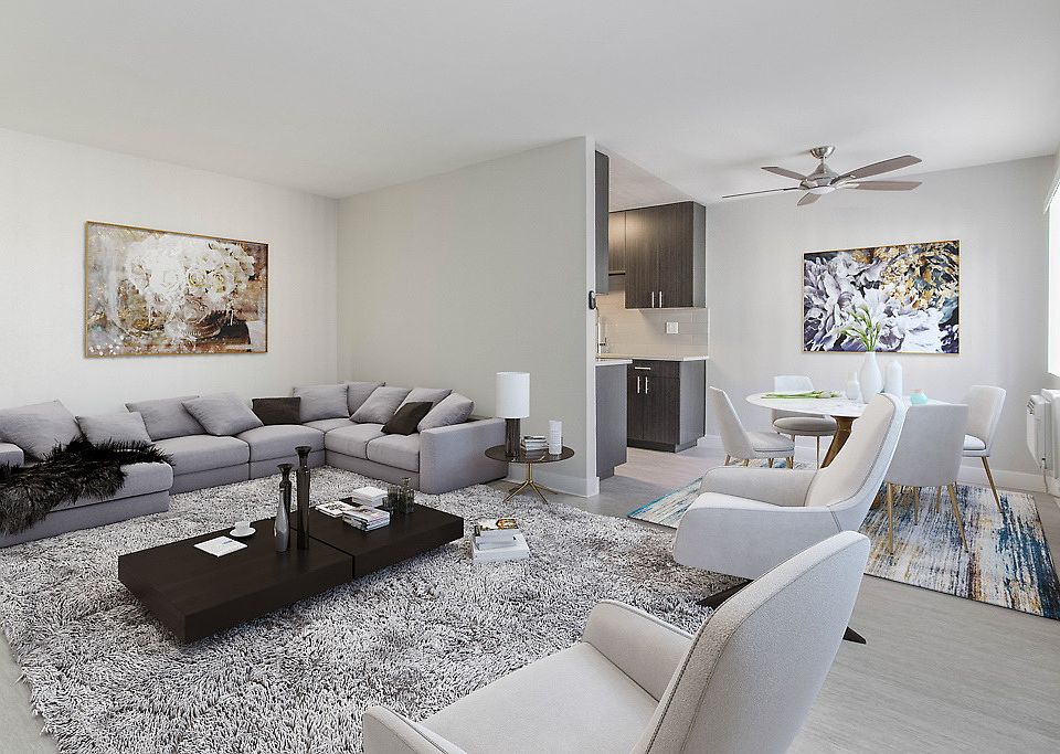 Staged living room adjacent to kitchen and dining area with a ceiling fan and large windows.