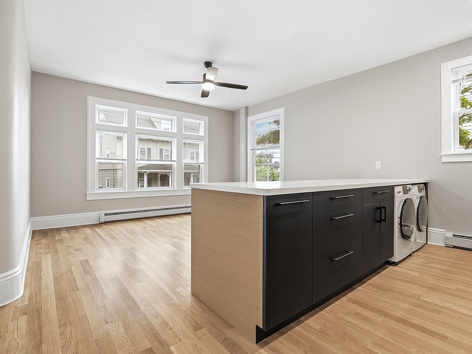 Contemporary kitchen featuring two-tone cabinetry, stainless steel appliances, white countertops, chef's sink, and light wood-finish flooring.