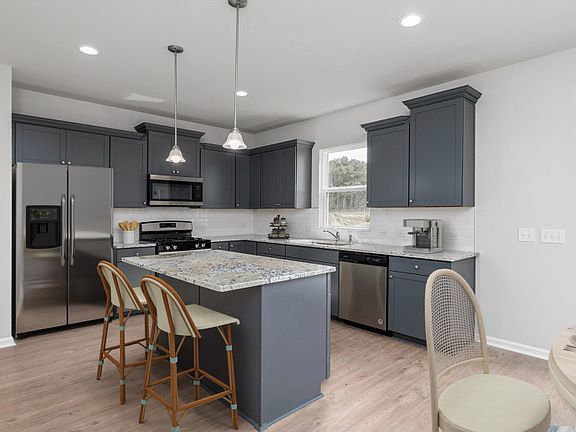 Beautiful gray cabinets with bright pendent lights above the large kitchen island. - Model Represen