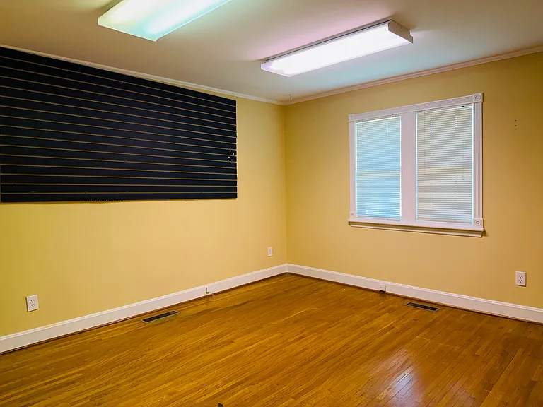 Bright, flexible room with warm neutral walls, natural light from the window and polished hardwood floors.