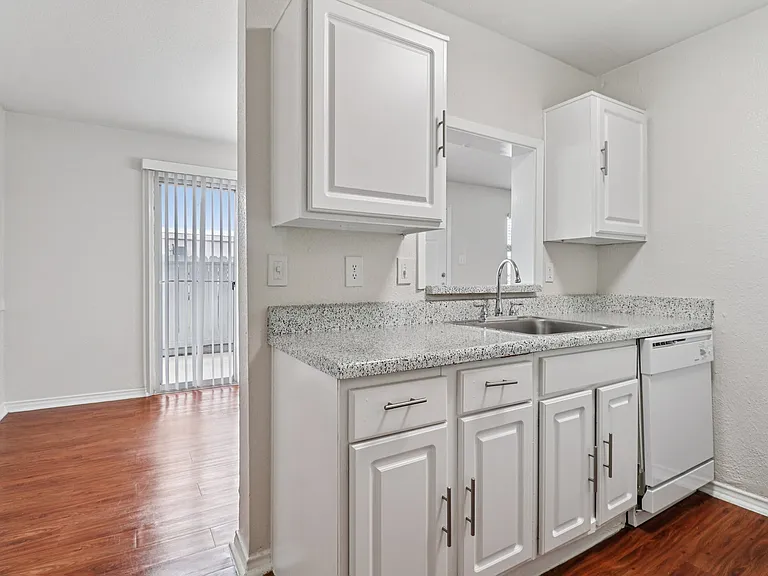 Charming kitchen with sleek speckled countertops, modern white cabinetry, and warm wood-style flooring with natural light streaming in. Charming kitchen with sleek speckled countertops, modern white cabinetry, and warm wood-style flooring with natural lig