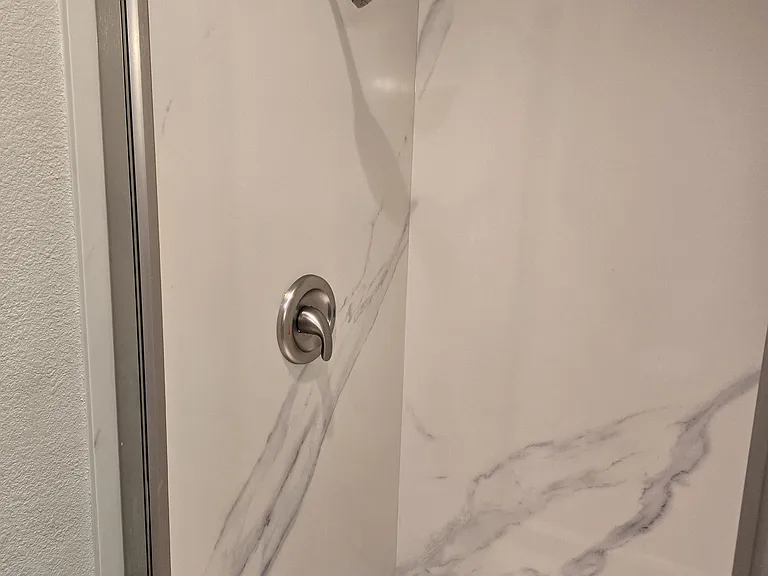 Spa-inspired walk-in shower with elegant quartz wall panels and contemporary brushed nickel fixtures.