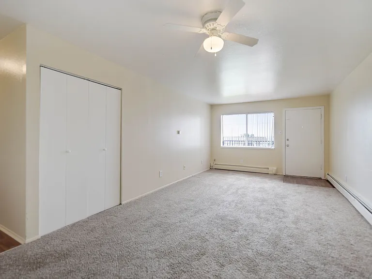 Bright and welcoming living space with plush carpeting, large window, and ceiling fan, perfect for relaxation.