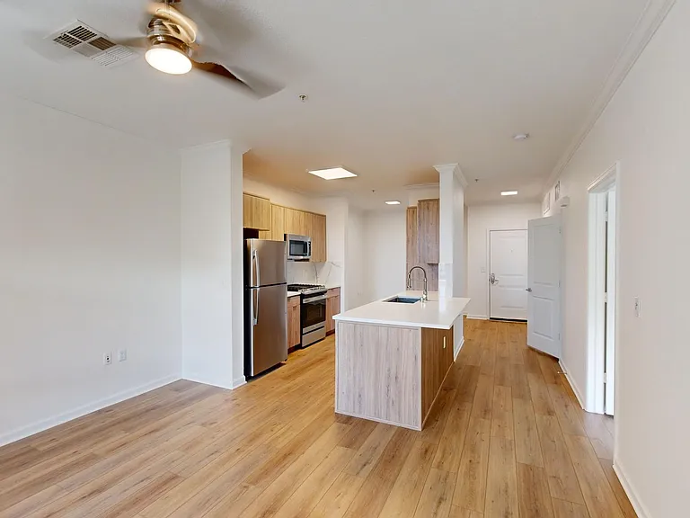 Apartment kitchen with stainless steel appliances and living room with wood style floor.