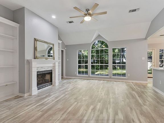 Living area w/ high ceilings, two large bookshelves straddling a wood-burning fireplace and large windows looking out to spacious patio and backyard