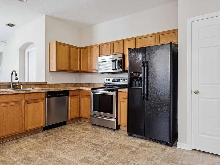 Kitchen has been updated with white cabinets and black handles, track lighting, and a stainless steel refrigerator
