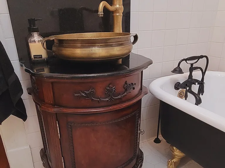 Beautiful brass vessel sink with black marble backsplash next to the clawfoot tub.