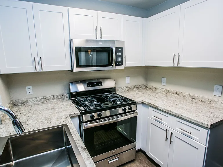 Stainless steel microwave and gas range with white shaker cabinets, granite counter, and large sink.