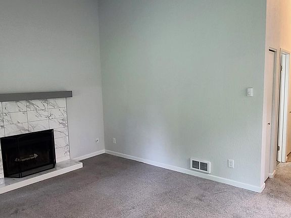 Living room with wood burning fireplace and new carpet, paint, window coverings and baseboards.