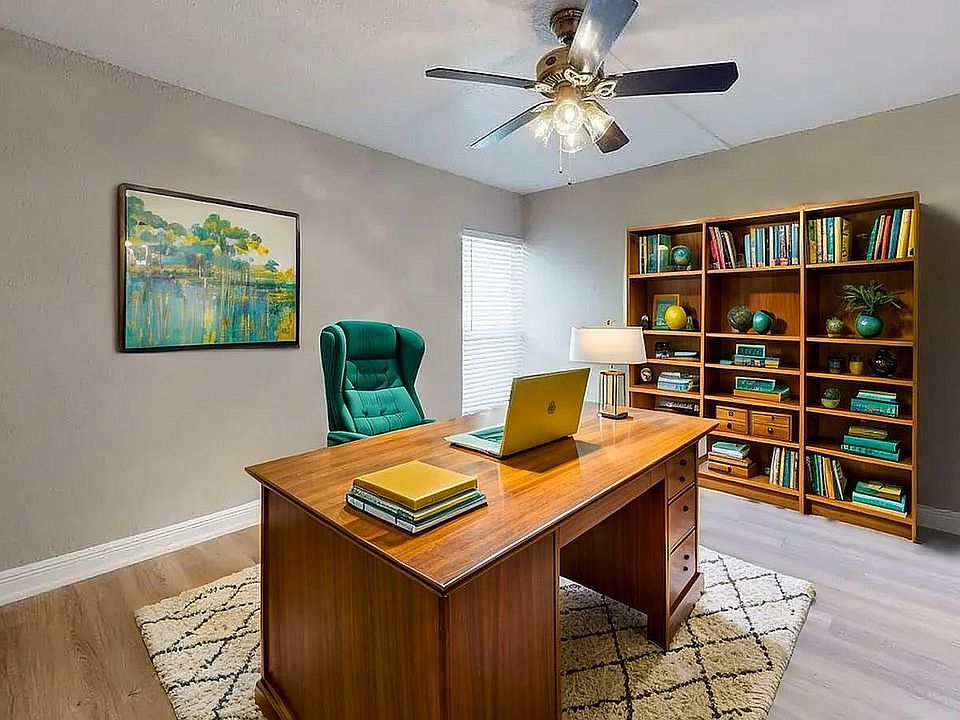 Elegant home office with a spacious wooden desk, plush green chair, and a cozy rug. Natural light enhances the inviting atmosphere, complemented by a well-organized bookshelf and modern decor.