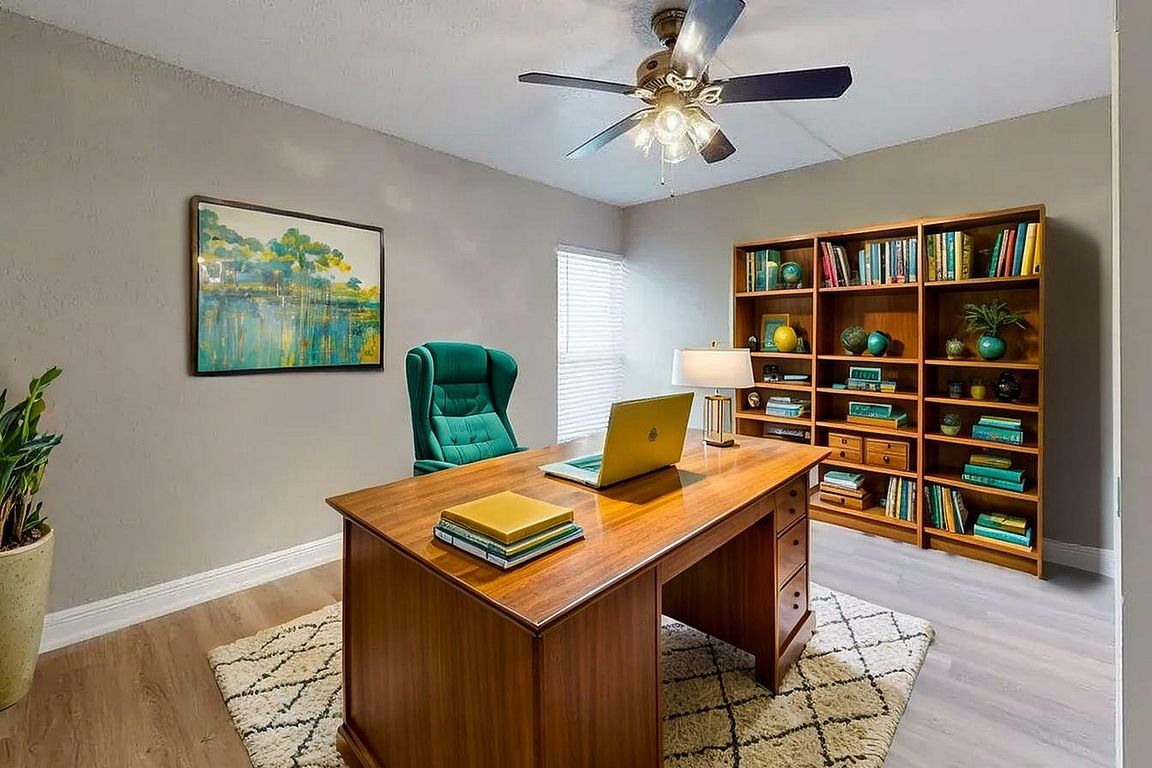 Elegant home office with a spacious wooden desk, plush green chair, and a cozy rug. Natural light enhances the inviting atmosphere, complemented by a well-organized bookshelf and modern decor.