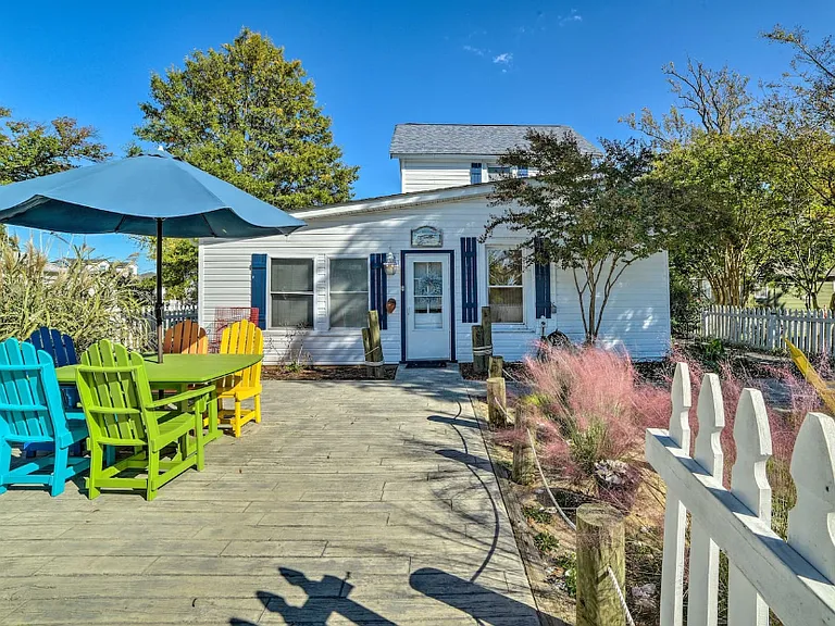 Front of the house, including the picnic table with colorful chairs and sun umbrella.