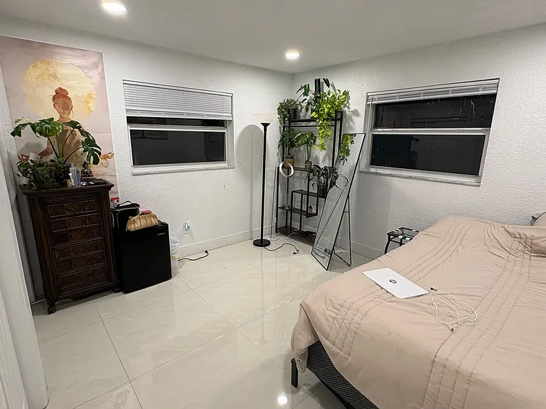 Spacious bedroom with tile floors, recessed lighting, and two windows with blinds for privacy and airflow.