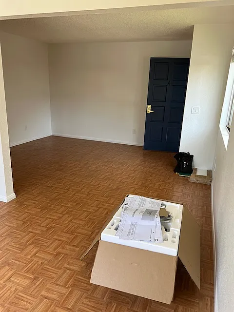 View from spacious dining area toward living room and front door. 
 Large window on right wall. The microwave is sitting in dining area in box, awaiting installation.