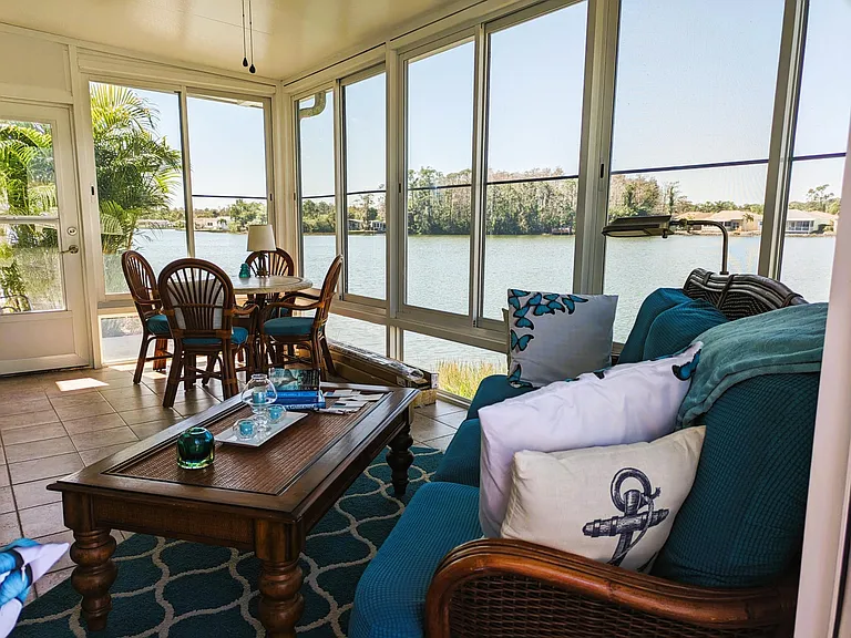 Full view of Beautiful lake front Lanai with sliding glass windows and screens, separate air conditioning unit, shades, couch + loveseat & kitchen table