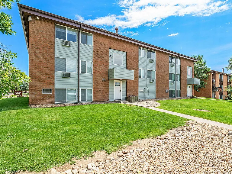 Charming brick apartment building with modern accents, surrounded by lush green lawns and a clear blue sky.