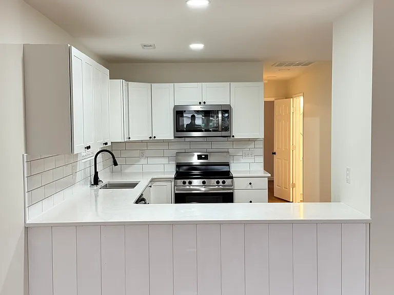 Modern open-concept kitchen featuring generous countertop space, abundant white cabinetry, subway-tile backsplash, stainless-steel appliances, built-in microwave, and a large peninsula perfect for dining or entertaining.