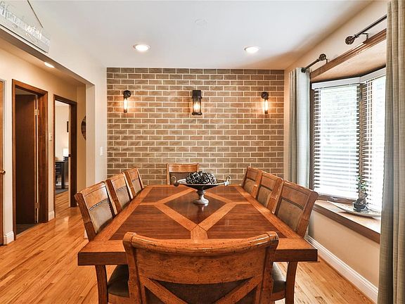 Large dining room with distinctive accent wall, bay window, attractive lighting and wood floor opens to entry foyer, living room and kitchen (across foyer)