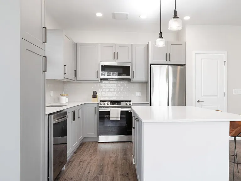 Modern kitchen with stainless steel appliances, white quartz countertop, light grey cabinetry, white tile backsplash, and hard surface flooring