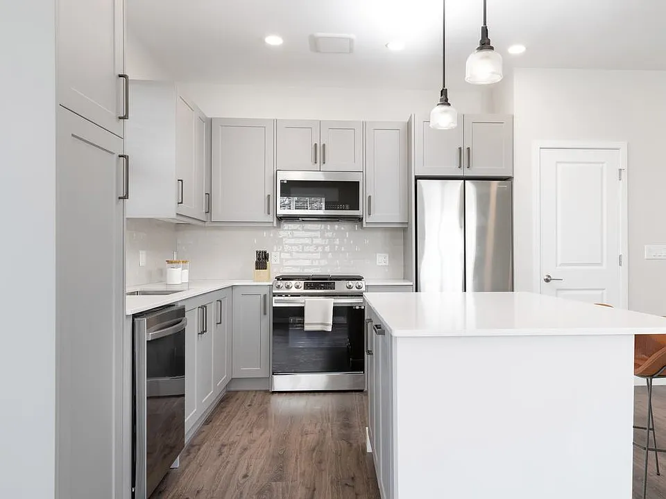 Modern kitchen with stainless steel appliances, white quartz countertop, light grey cabinetry, white tile backsplash, and hard surface flooring