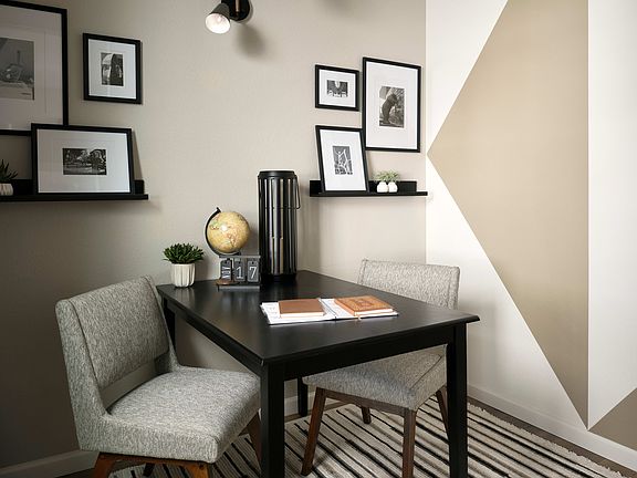 A modern and minimalist home office space with a dark wooden desk, gray upholstered chairs, and fram