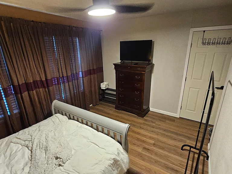 Furnished bedroom with bed, dresser and TV, plus closet storage and durable flooring for easy upkeep.