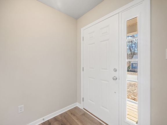 A white front door with an adjacent vertical window panel. The interior features beige walls and woo