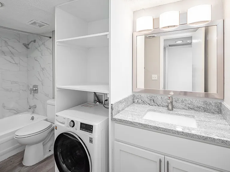 Bright bathroom with granite counters and bathtub with marble backsplash
