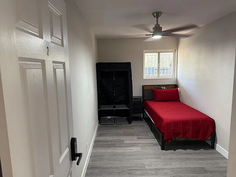Private bedroom with a ceiling fan, wood-look flooring, and a window for natural light, plus space for a bed and storage.