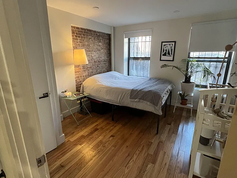 Bedroom with hardwood floors, exposed brick accent wall, and two windows for natural light and ventilation.