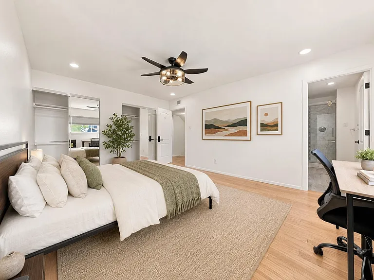Spacious bedroom with hardwood floors, ceiling fan, mirrored closet doors, a desk nook, and an en-suite tiled shower.