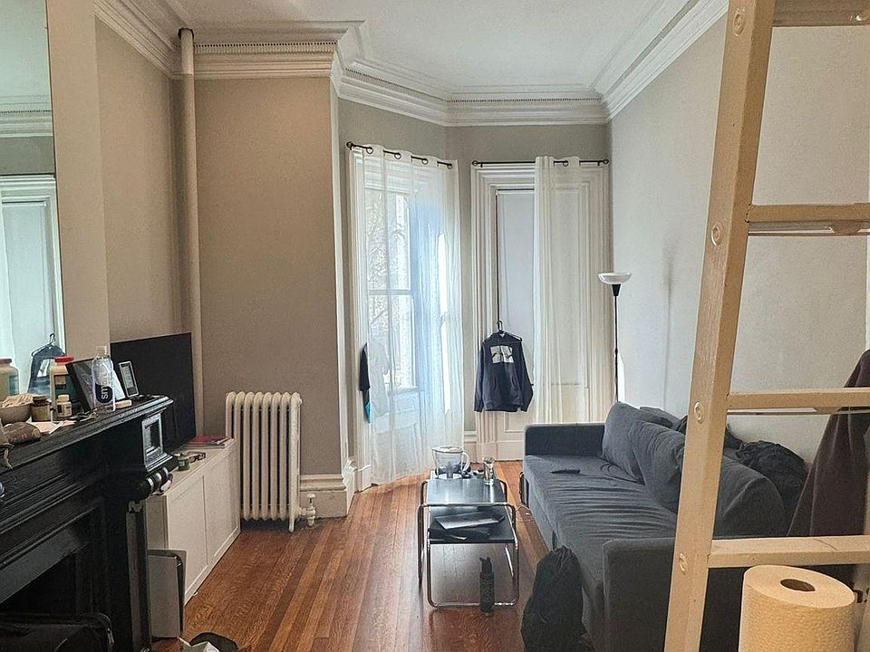 Living space with the bay window, sofa-bed, black fireplace, and TV. The wooden bed-platform is on the top and the ladder is also shown.