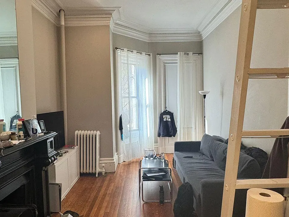 Living space with the bay window, sofa-bed, black fireplace, and TV. The wooden bed-platform is on the top and the ladder is also shown.