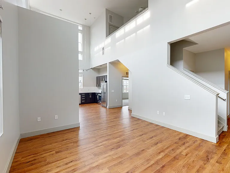 Apartment kitchen with stainless steel appliances, dining and living room with wood-style flooring.