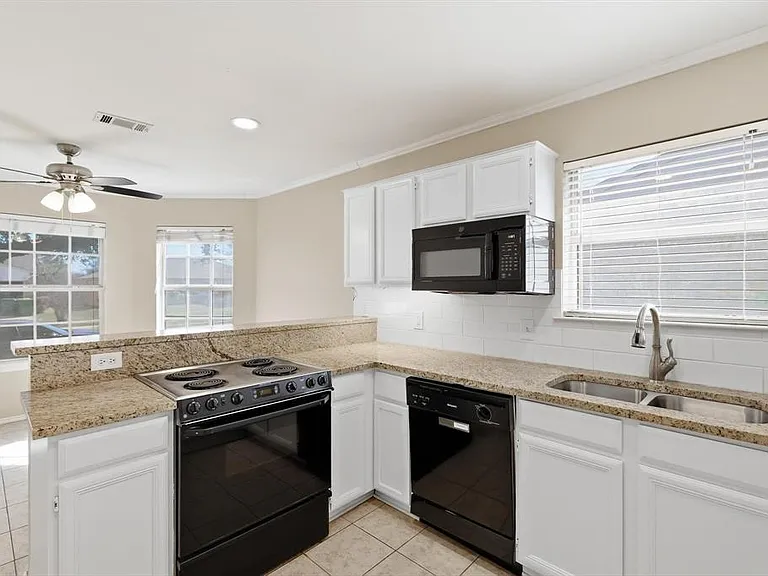 Kitchen featuring black appliances, a peninsula, tasteful backsplash, white cabinetry, and plenty of natural light