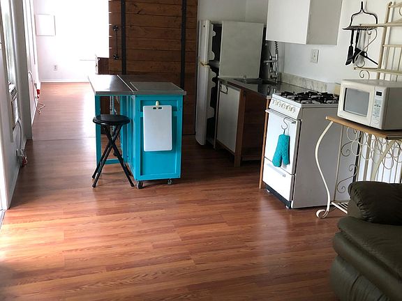 Kitchen has overhead hanging rack for pots & pans, refrigerator, sink, stove/oven, microwave