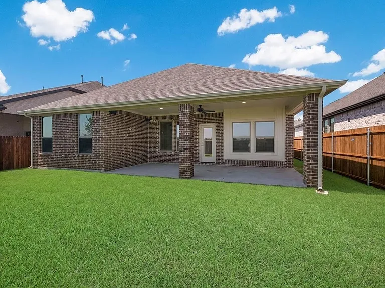 Expansive backyard featuring a manicured lawn, brick exterior, covered patio, and a privacy fence