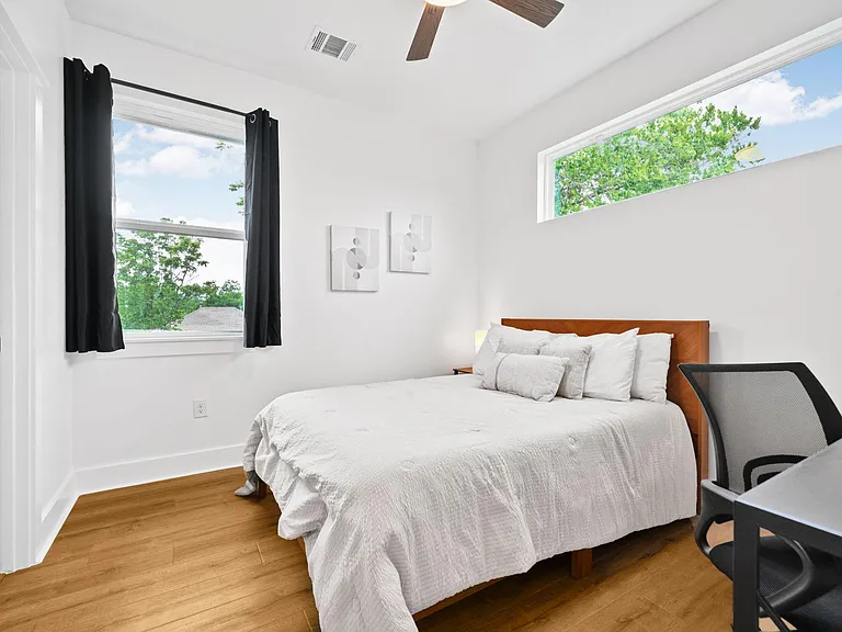 Bedroom with hardwood floors, ceiling fan, two windows, and space for a desk alongside the bed.