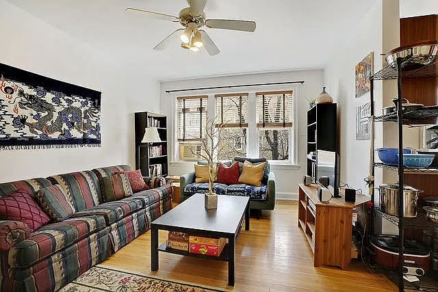 Living room has sunny windows facing residential street and trees, and hardwood floors, new paint