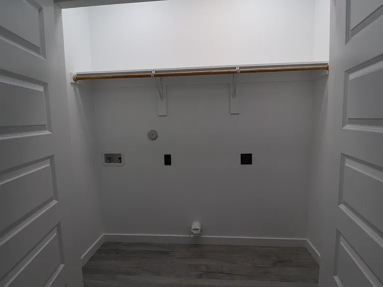 Spacious laundry room with washer and dryer connections, storage shelf, and hanging rod.