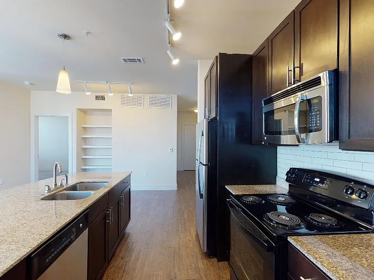 Apartment kitchen with granite countertops and wood-style flooring.