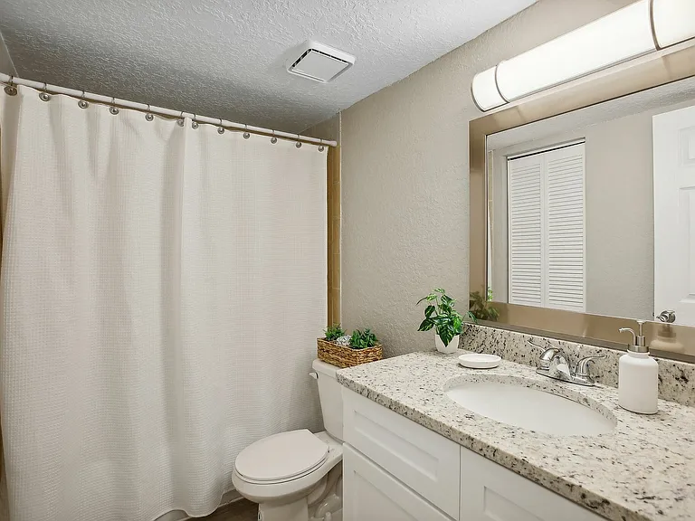 Elegant bathroom with a modern design featuring granite countertops, a large mirror, and natural accents, offering a serene and inviting atmosphere.
