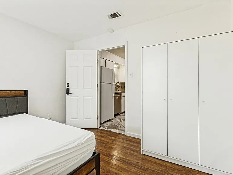 Private bedroom with hardwood-style floors, furnished bed, and large double-door closet near the kitchen area.