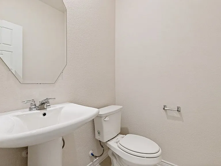 Pedestal sink with chrome faucet, octagonal frameless mirror, and white toilet