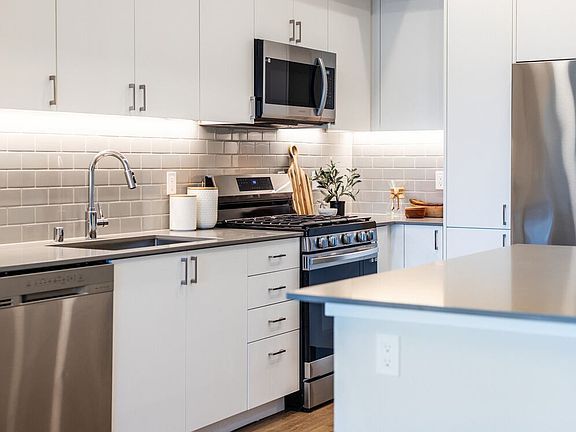 Kitchen with grey quartz countertops, white cabinetry, grey subway tile backsplash, stainless steel appliances, and hard surface flooring
